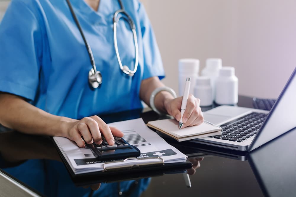 Healthcare costs and fees concept. A doctor's hand uses a calculator, smartphone, and tablet to manage medical expenses at the hospital.