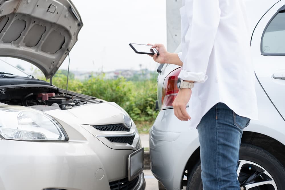 A male driver inspects the damage after a car accident before taking photos for evidence.