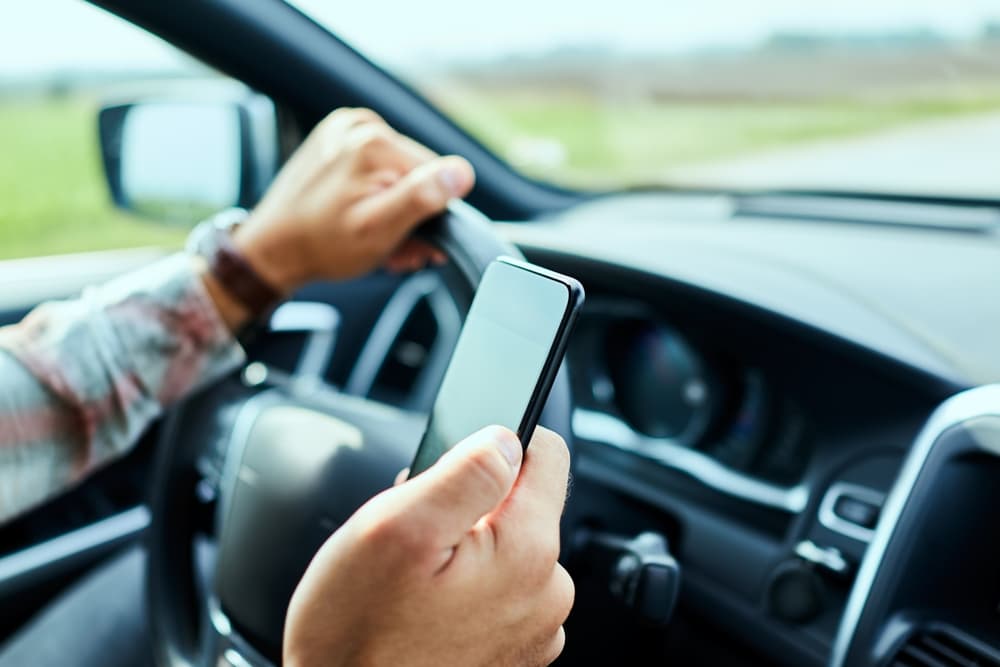 Man using a smart phone while driving a car on the road