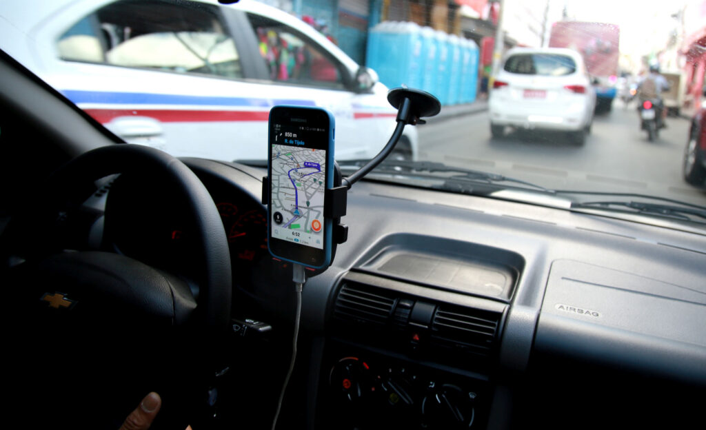 View from inside a vehicle's dashboard showing a smartphone mounted next to the steering wheel displaying a GPS navigation route on a busy city street, illustrating rideshare driving tools reviewed by a Port Richey Uber accident attorney at Nicoletti Injury Lawyers.